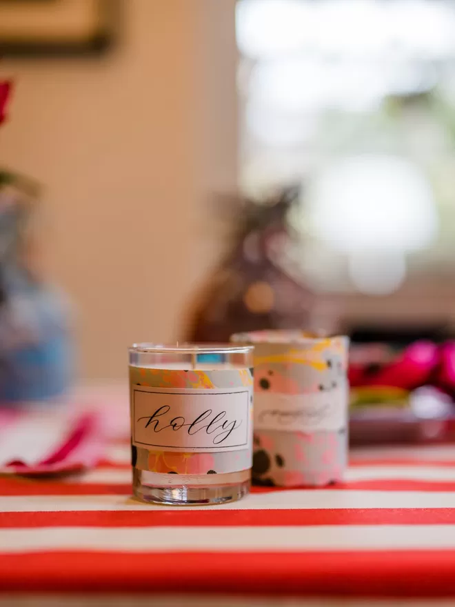 Sassigraphy Hand Poured Scented Candle With Personalised Marbled Label seen on a red and white striped table coth.