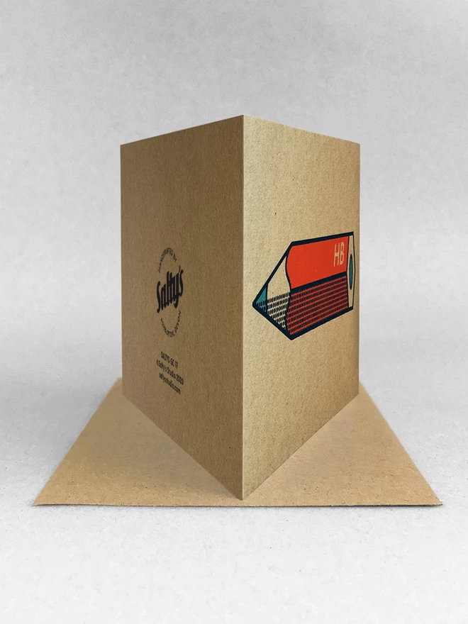 Rear view of a red pencil design on brown Kraft card, with black outline and half tone detail. Stood on a Kraft brown envelope in a light grey background with soft shadows