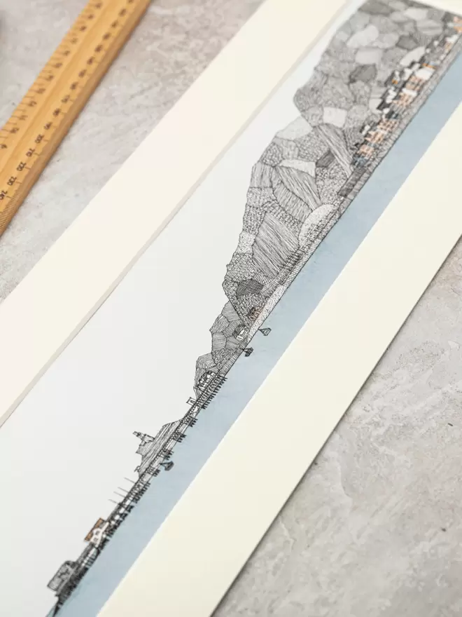 Detailed pen and watercolour drawing of Mumbles pier and seafront, with mountain backdrop, in a soft white mount