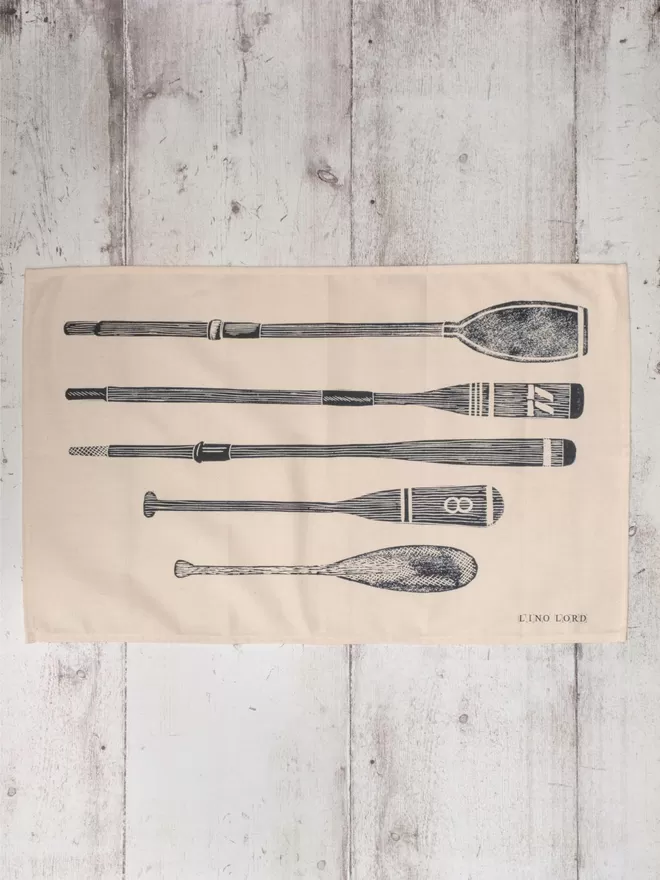 Picture of a tea towel with an image of oars and paddles, taken from an original lino print