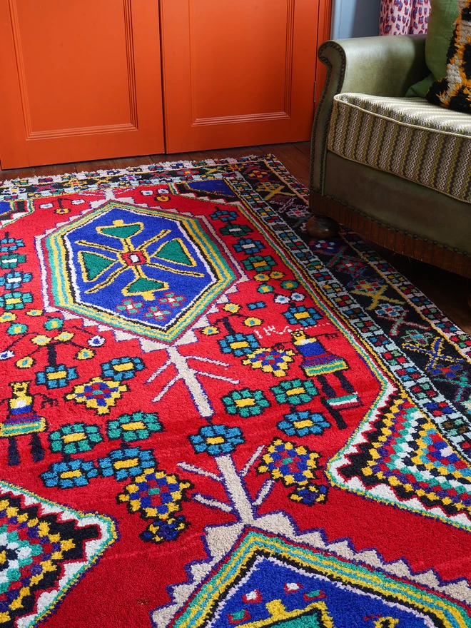 Brightly coloured Persian vintage rug, in a red, green and blue pattern in a bedroom with orange wardrobe,  and iron bed