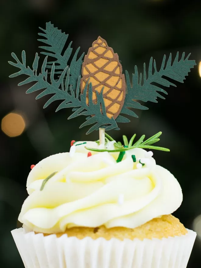 Spruce Christmas paper cupcake topper including a two-toned brow pinecone and three pieces of dark green spruce.