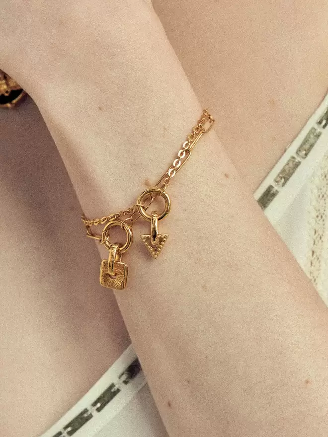 woman wearing two gold bracelets styled with a doradus star charm and triangle charm