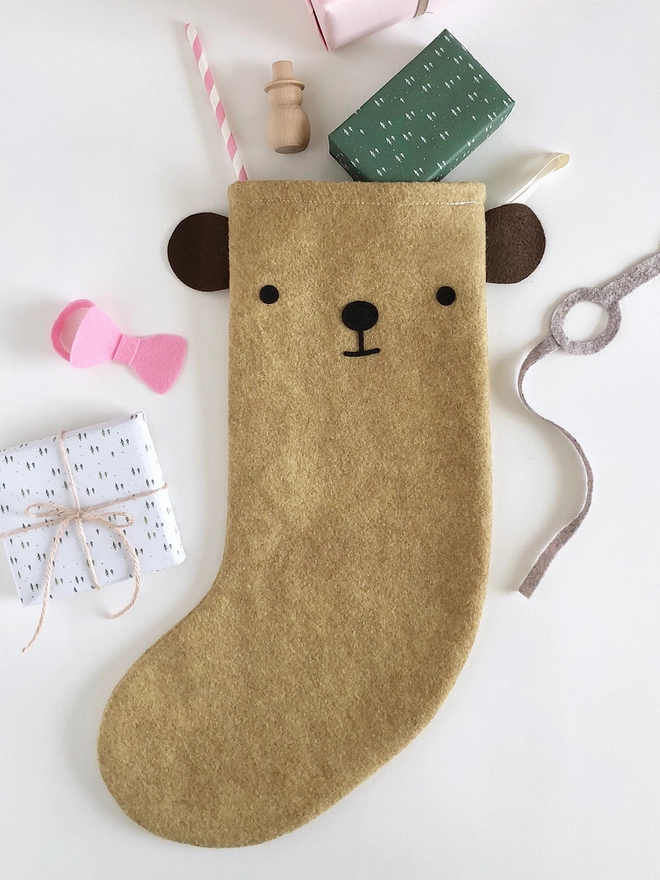 A handmade felt bear stocking lays on a white surface with several gifts poking out from the top.