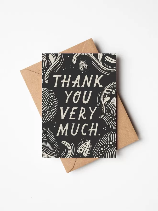 Black and white greeting card with illustration and the words thank you very much written on it lay a brown envelope on a white surface