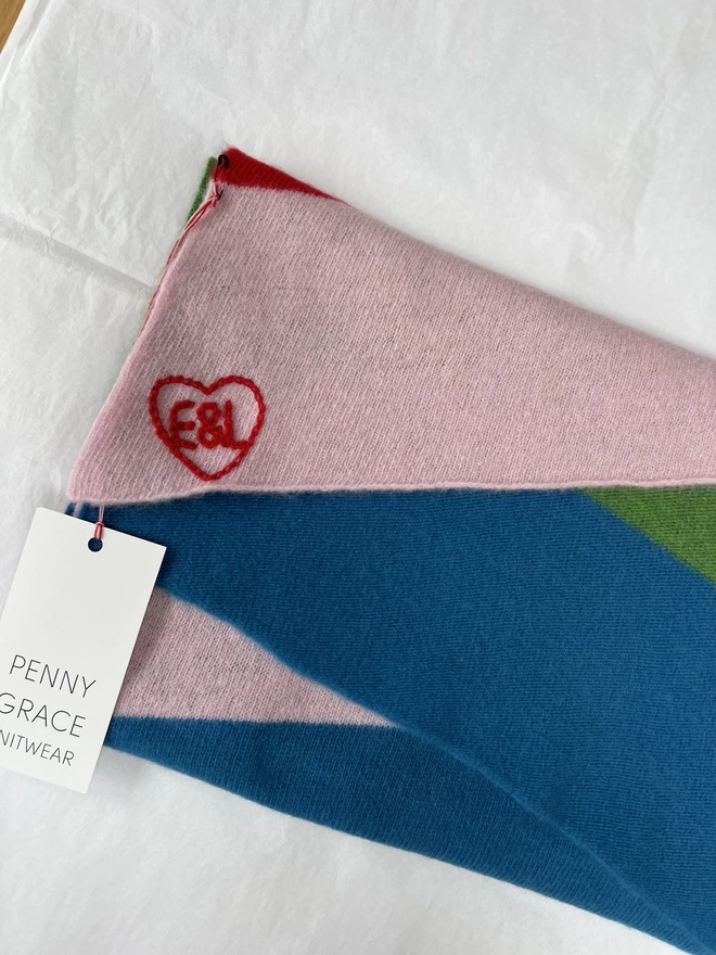 Rainbow stripe scarf folded, and showing embroidered heart with initials