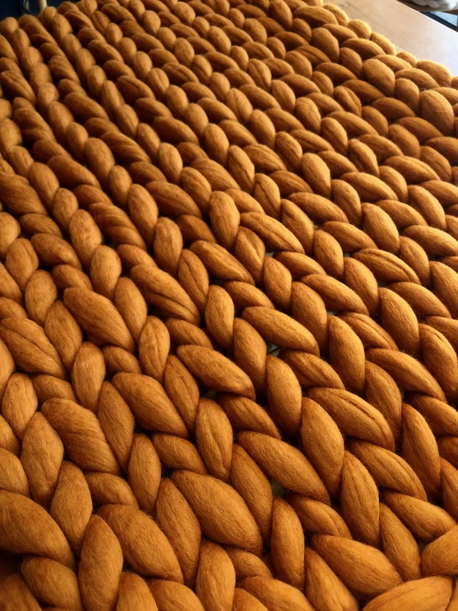 A close up of the stitches of a giant knitted merino blanket in amber 