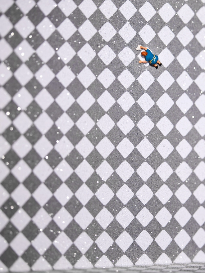 Miniature scene in an artbox showing a tiny cleaning lady washing a vast checkerboard floor 