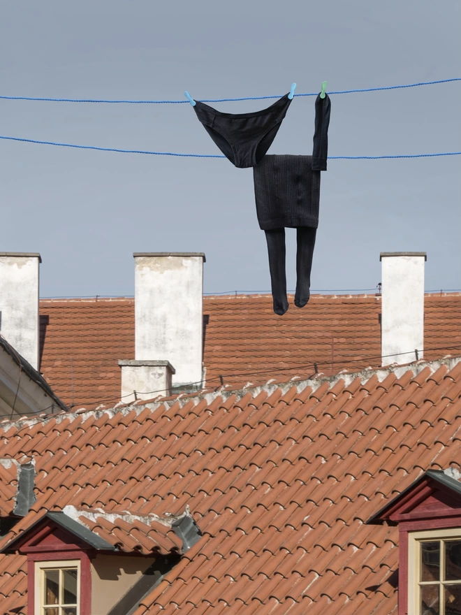 Inky the cat made of laundry, hung on a clothes line above some houses