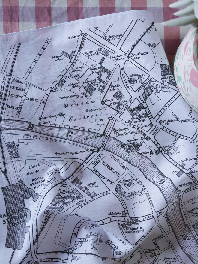 A lifestyle photo of a Mr.PS York Map hankie on a gingham tablecloth with a plant pot