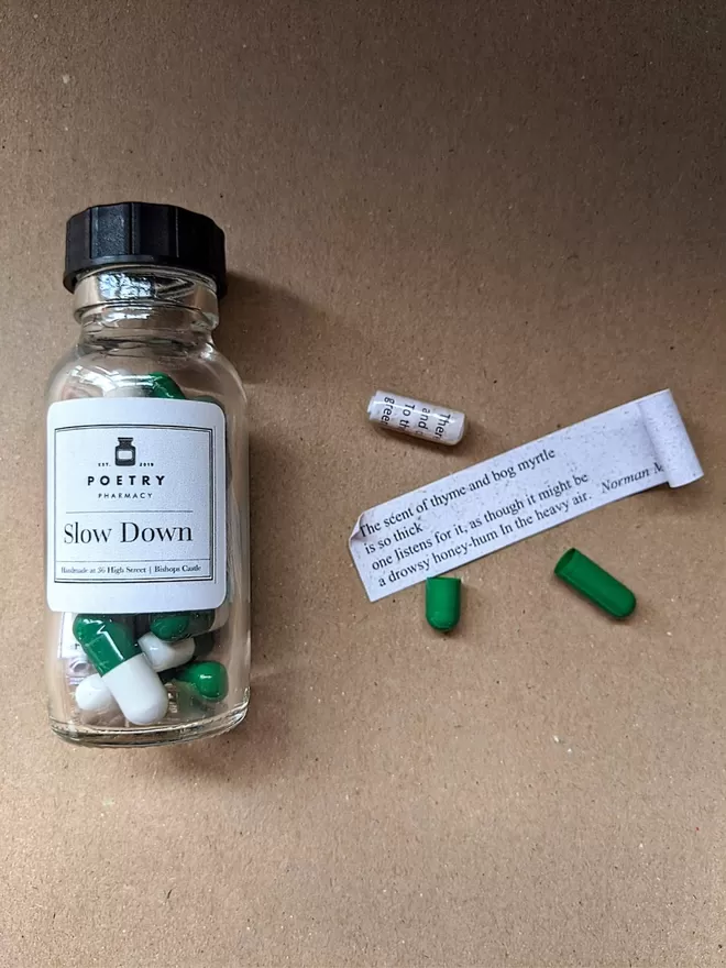 Glass pill bottle containing green and white Slow Down poetry pills printed on banana paper