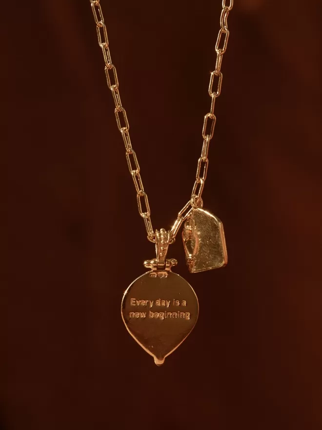 Back of pendant with engraved message Every day is a new beginning against dark red background
