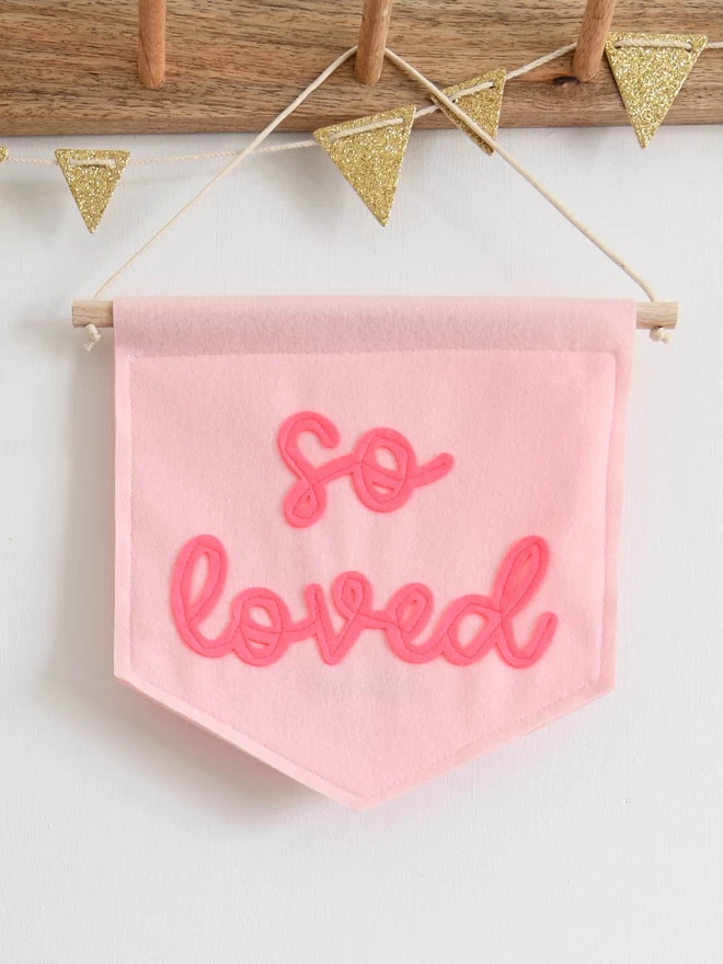 pink felt banner with so loved sewn on in cursive font.