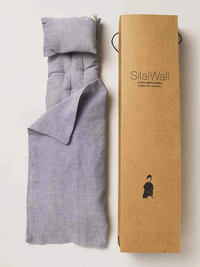 Cardboard box with Silaiwali logo next to a quilted doll's mattress, pillow and sheet all in a navy and white pinstripe design