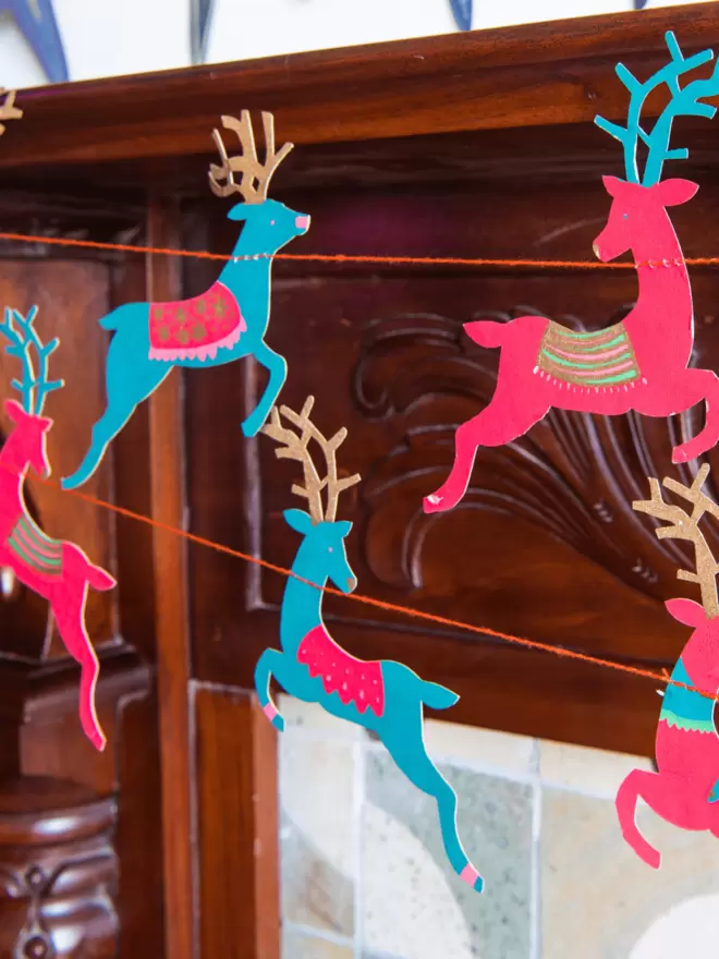 Teal and pink reindeer shapes hung on wooden fireplace