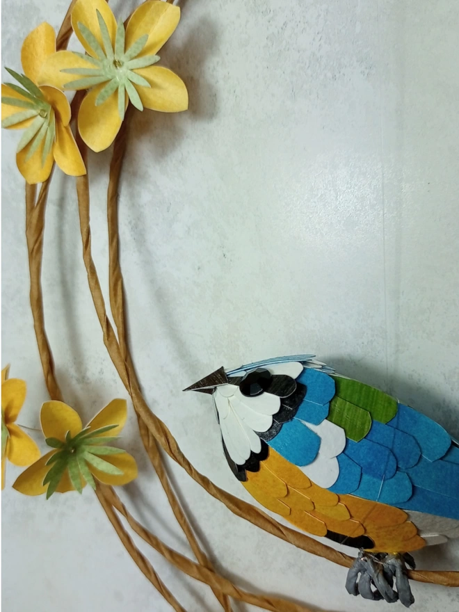 Close up of a blue tit sculpture, with yellow paper flowers.