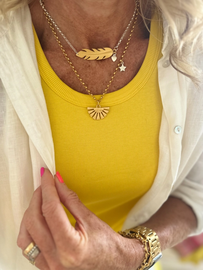 model wears a gold plate feather charm on a sterling silver chain with additional silver mini heart