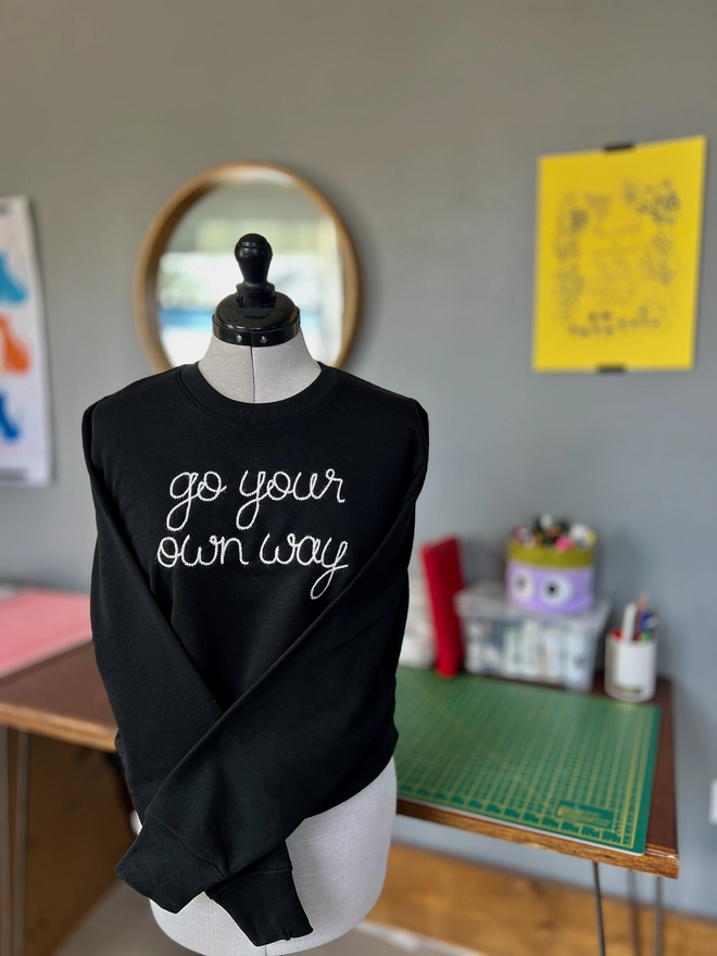 A black sweatshirt on a dressmakers form embroidered with go your own way