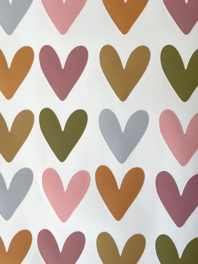 Close up of sheet of muted rainbow coloured heart shaped wall stickers