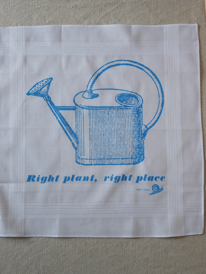 A Mr.PS Watering Can hankie laid flat on a linen tablecloth