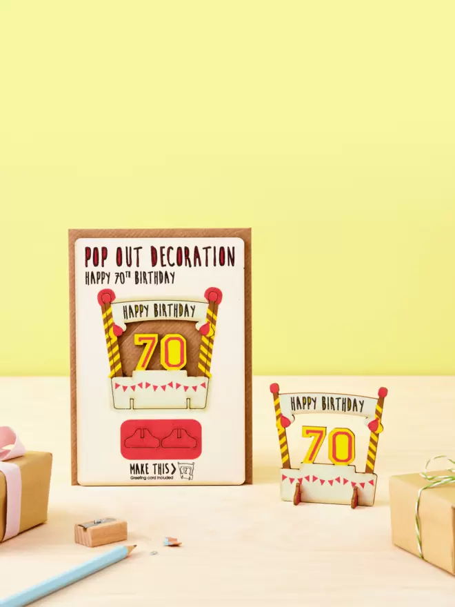 Pop out seventieth birthday decoration and seventieth birthday card and brown kraft envelope displayed on a wooden desk