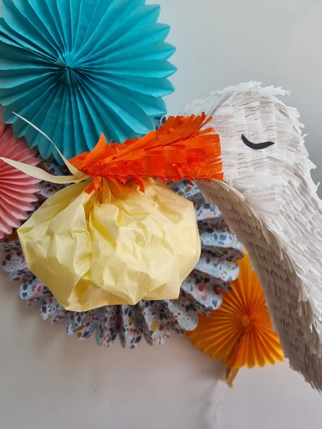 close up of the stalk pinatas face with closed eyes and a baby bundle in its beak