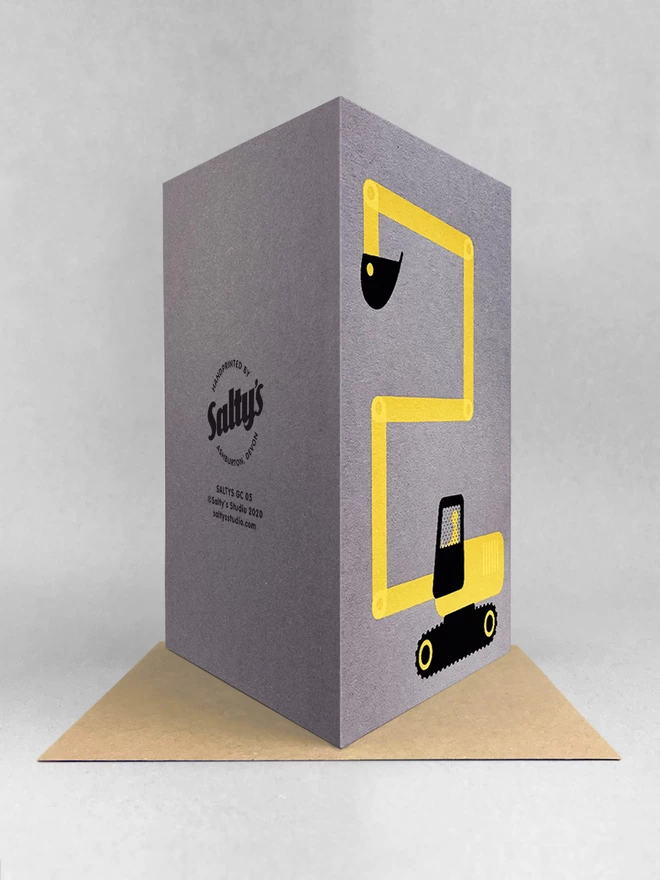 rear view of a digger card making a number 2 with its digger arm, screenprinted in yellow and black ink on a grey cardstock. stood on a brown kraft envelope in a light grey background. 