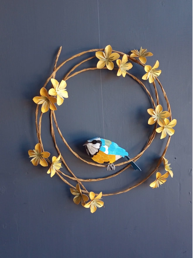 Blue tit bird sculpture, perched on a wreath of yellow blossom flowers.