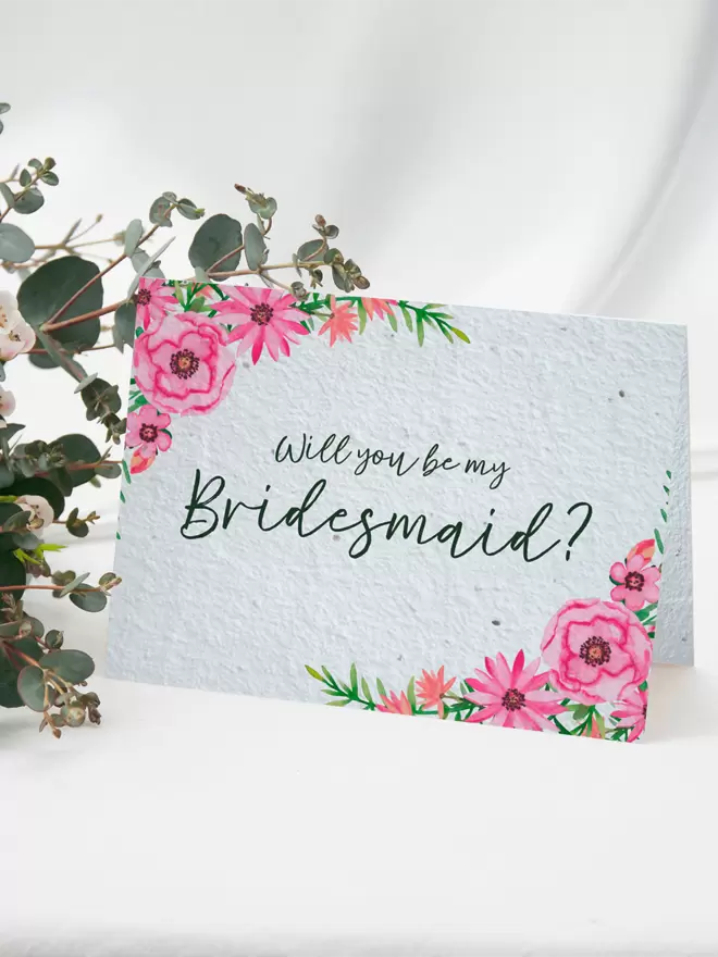 Seeded Paper Greeting Card featuring floral illustrations with ‘Will you be my Bridesmaid?’ written in the centre with a bunch of flowers in the background