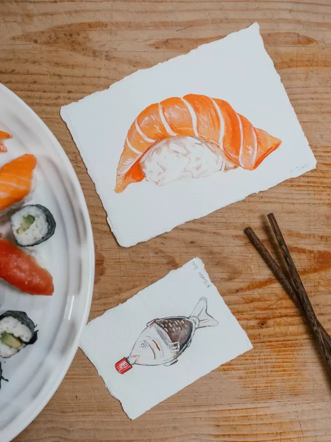 Katie Tinkler Salmon Sushi seen on a wooden table with sushi and a soy sauce illustration.