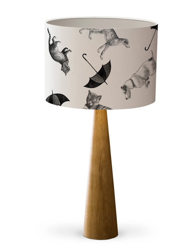 Drum Lampshade featuring cats and dogs ‘raining’ from the sky with a white inner on a wooden base on a white background