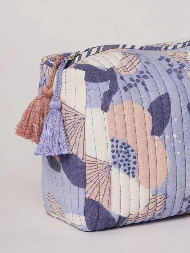 Detail of two tassels, one soft blue and one dusty pink hanging from the side of a blue block printed floral washbag