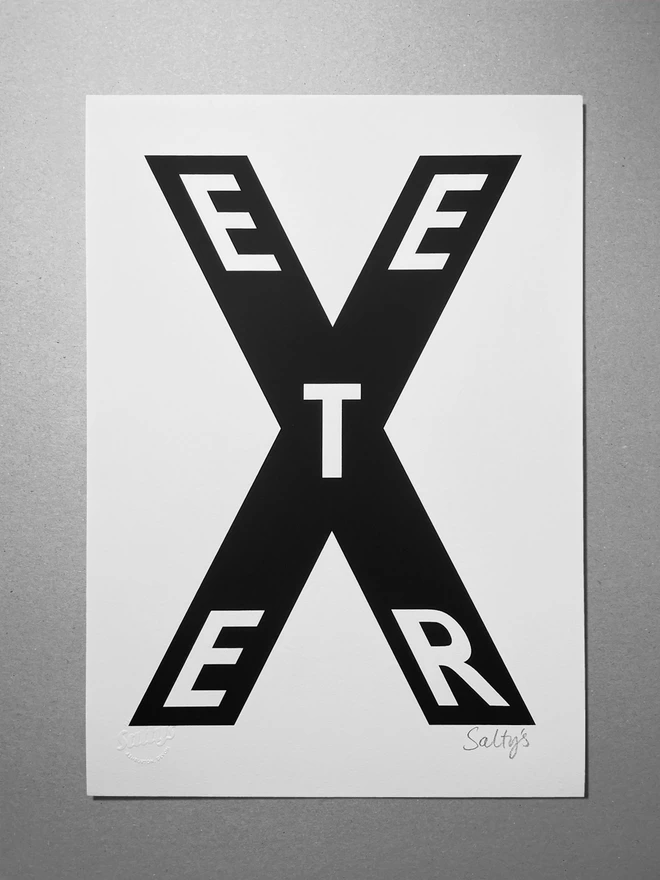 Full view of the Exeter print, an X fills the page with the letters spelling Exeter spread through the main letter. Black ink on white paper. The print is laid on a greyboard background