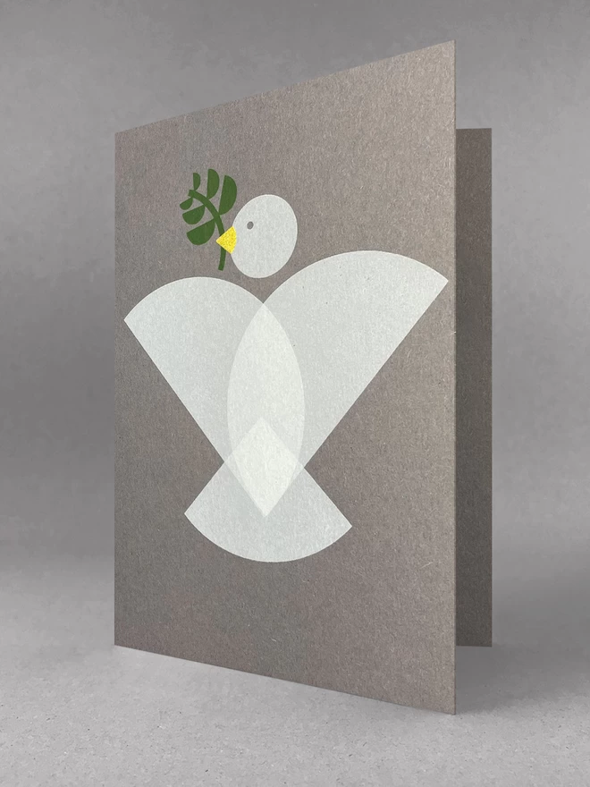 Geometric shapes make up a dove design on this handprinted christmas card, with an olive branch and gold beak. Stood slightly open in a studio set.