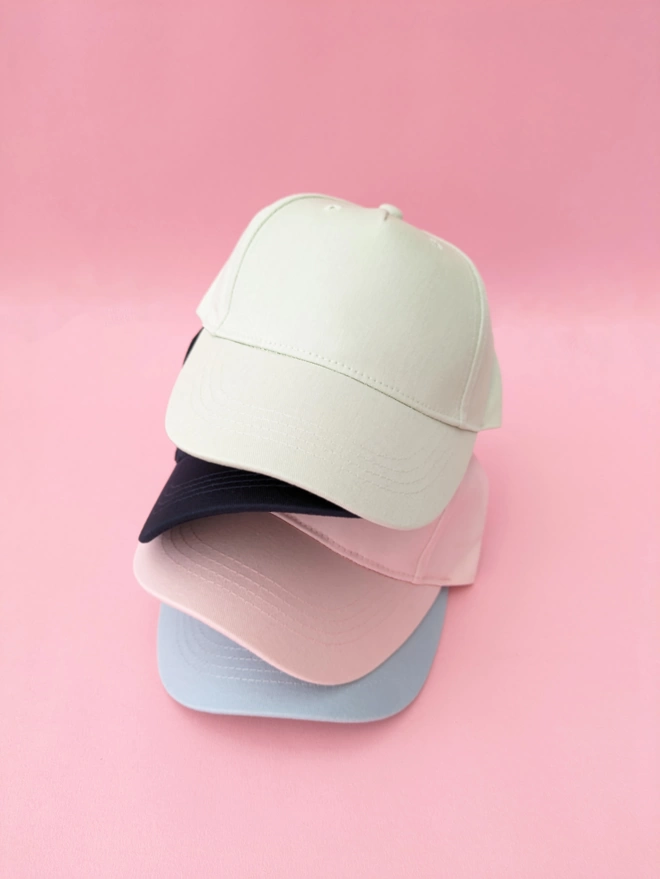 A stack of kids baseball caps in Powder Pink, Blue & Pistachio Green. 