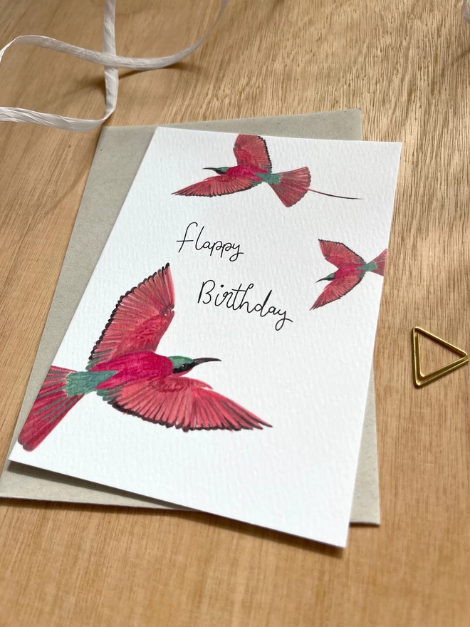 a greetings card featuring three pink carmine bee-eater birds with the phrase “flappy birthday”