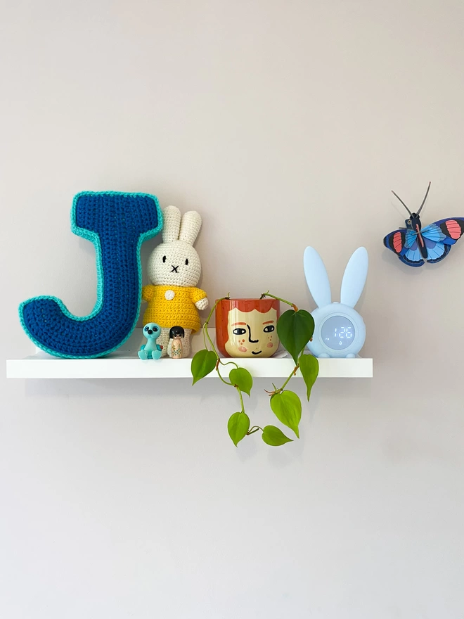 Crochet J Cushion in Blue and Teal, on a child's shelf
