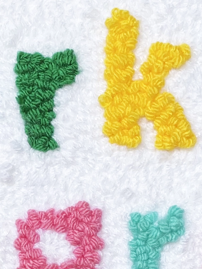 green letter "r" and yellow letter "k" in punch needle wool on a white background