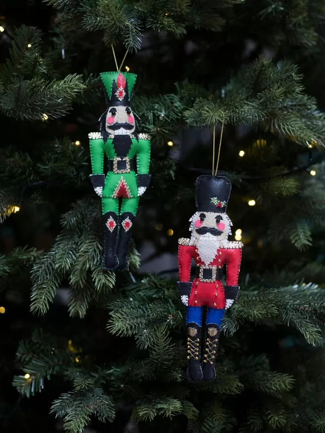 Hetty and Dave leatherette nutcracker decorations hanging on a Christmas tree, one is green, the other red