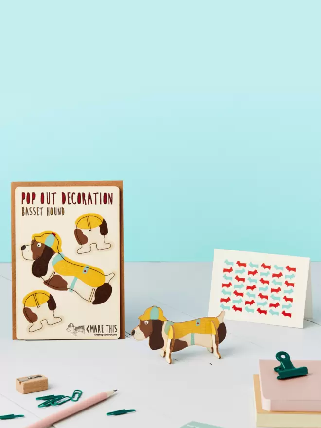 3D basset hound decoration and basset hound pattern greeting card and brown kraft envelope on top of a grey desk in front of a light blue coloured background