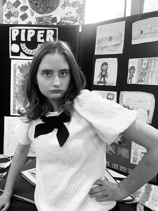 Black and White photo of Piper with her hand on her hip in front of a display of art 