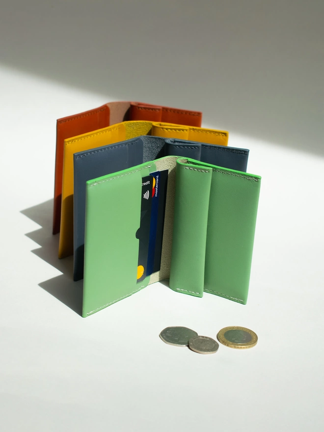 Coin Wallets in Sea Green Dark Green, dark green, amber yellow and rust brown coin wallet respectively. The closest wallet is in sea green with cards inside. There are some coins outside scattered outside