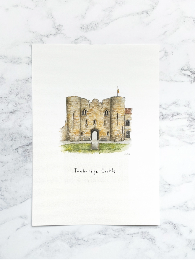 Beautiful watercolour illustration of Tonbridge Castle, Tonbridge, Kent.  A wonderful sandstone coloured castle with two turrets either side of an arched entrance. A flag sits at the top and to the left a slightly eroding wall. The green castle lawn and steps down to the grass sit in front of the arch. The watercolour style is painted with a black pen outline and organic loose style with small details. The print is a small illustration on the centre of a white page and the paper sits on a white marble background.