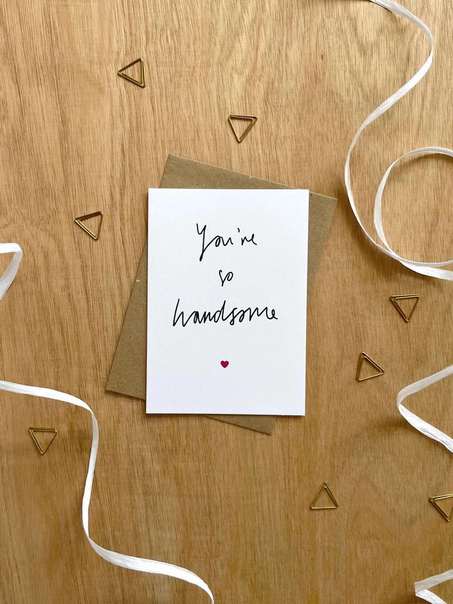 a simple greetings card featuring hand drawn text saying “you’re so handsome” with a tiny pink heart