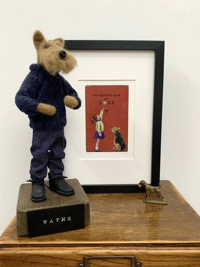 a framed print of an airedale or welsh terrier with a little girl and tennis ball painted onto the observer book of dogs in a black frame