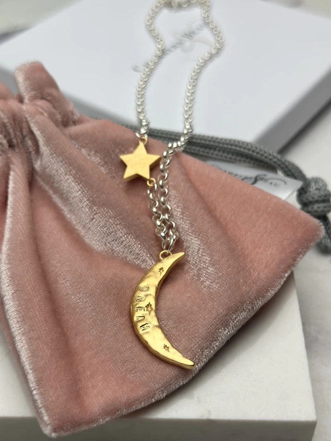 a rough hewn gold plate moon charm hangs from a sterling silver chain. inset in the chain is a chunky gold cosmo star charm