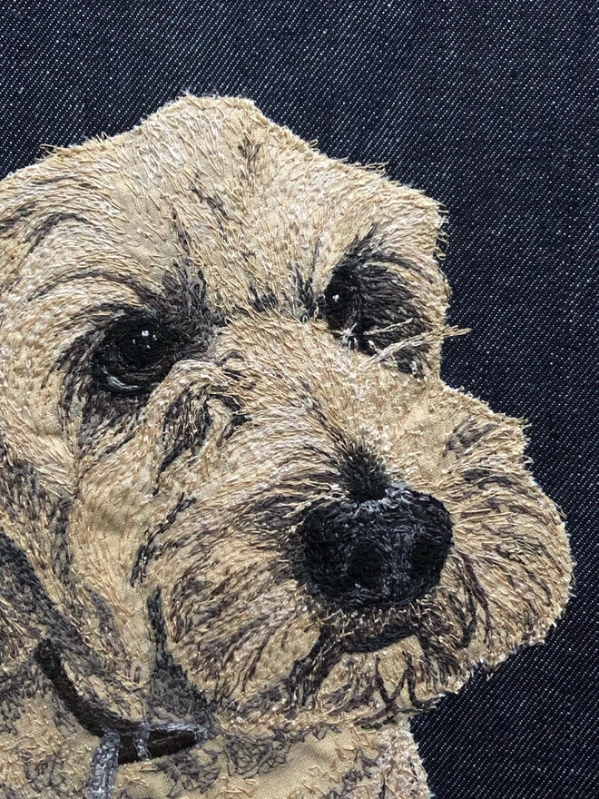 detail of an embroidered pet portait of a cockerpoo on a plain denim background