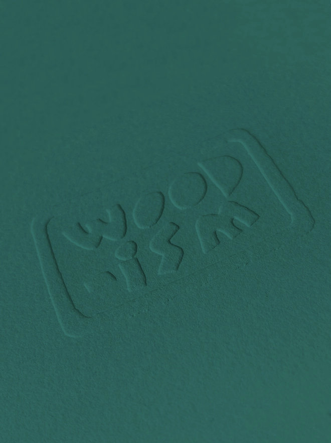 A close up of the Woodism logo embossed on a green paper