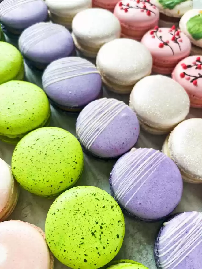 many different coloured spring themed macarons are arranged on a tray