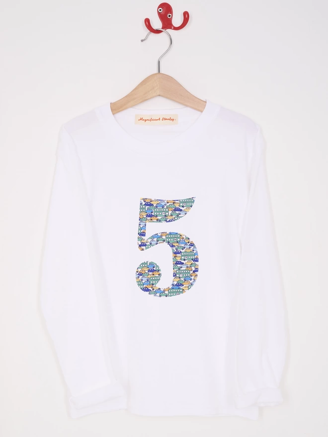 A white cotton long sleeve t-shirt appliquéd with the number 5  in Liberty print featuring vintage cars and busses hanging on a hanger 